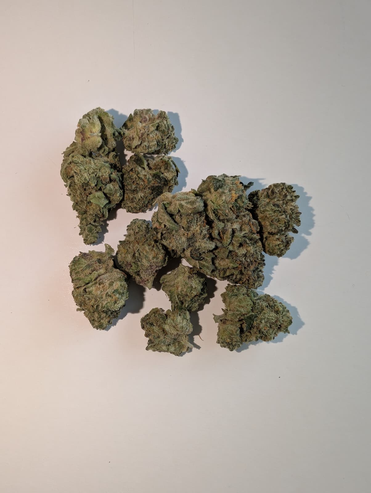 Several dried green cannabis buds clustered together on a plain off-white background.